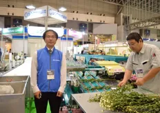Kenta Yoshihara of Shinwa standing in front of the flower classifying and binding machine. First the flowers are put on the machine. Then the leaves are being removed and they are being classified by weigt. They they are grabbed and binded.